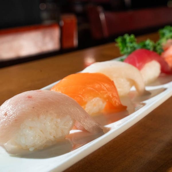 A white rectangular plate holds five pieces of colorful nigiri sushi on a wooden table.