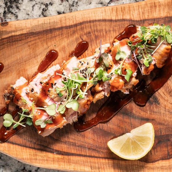 Sliced steak or sushi, drizzled with sauce and garnished with microgreens and a lemon wedge.