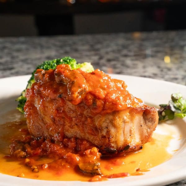 Birkin's Steakhouse pork chop with red sauce, broccoli, and a side salad on a white plate.
